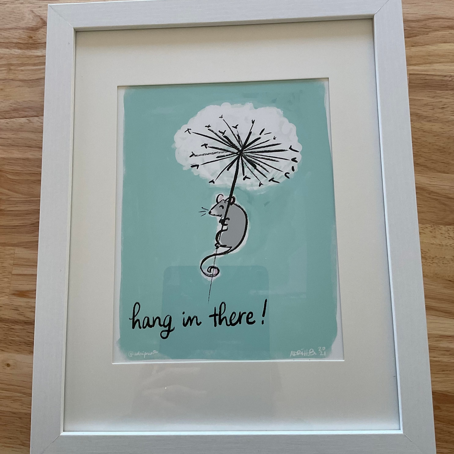 Framed art print featuring a stylized mouse and dandelion on a teal background with the phrase 'hang in there!'
