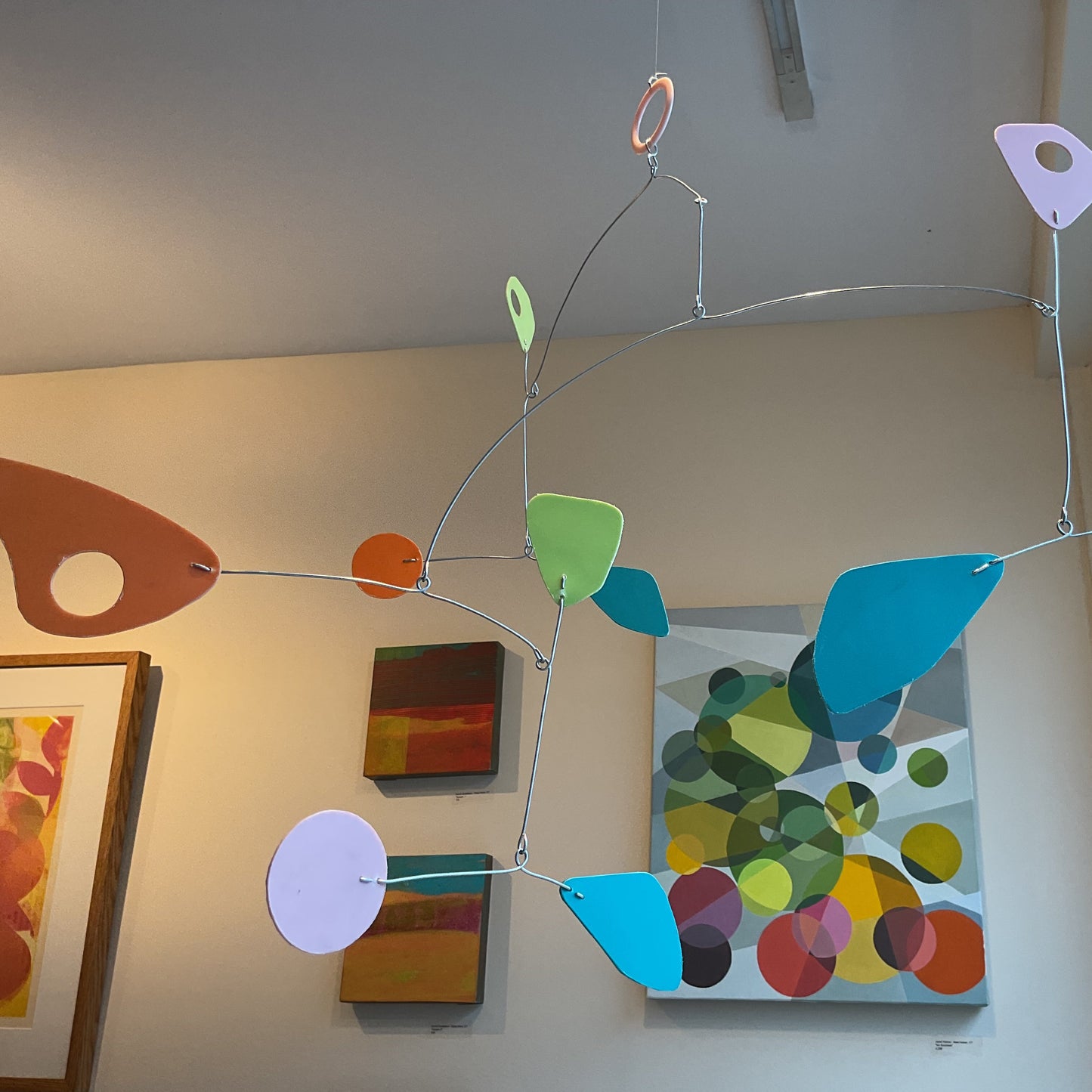 A colorful mobile made of paper or cardboard cutouts in various shapes, including circular and triangular, suspended by a string, displayed indoors.