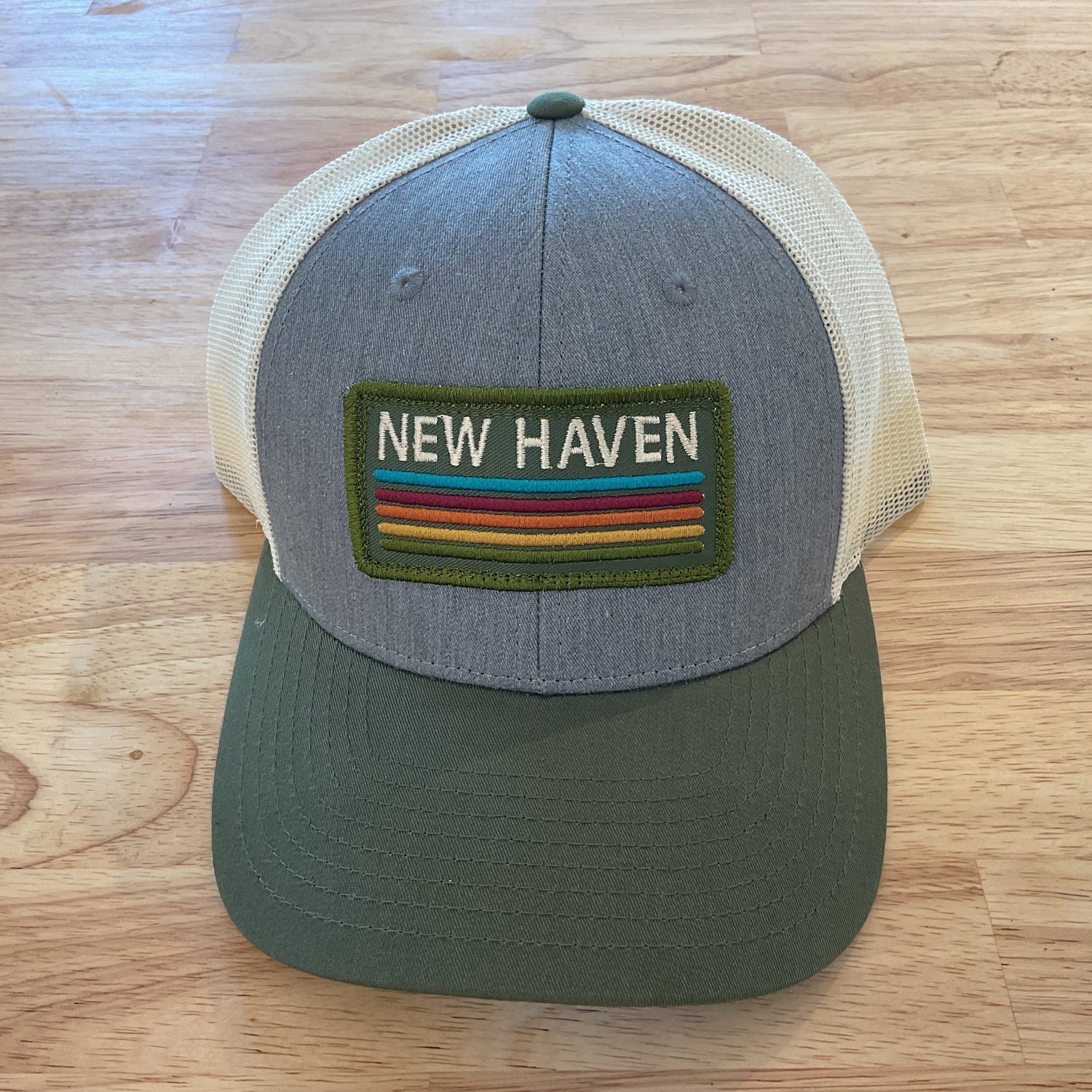Gray and green cap with 'New Haven' patch on a wooden surface