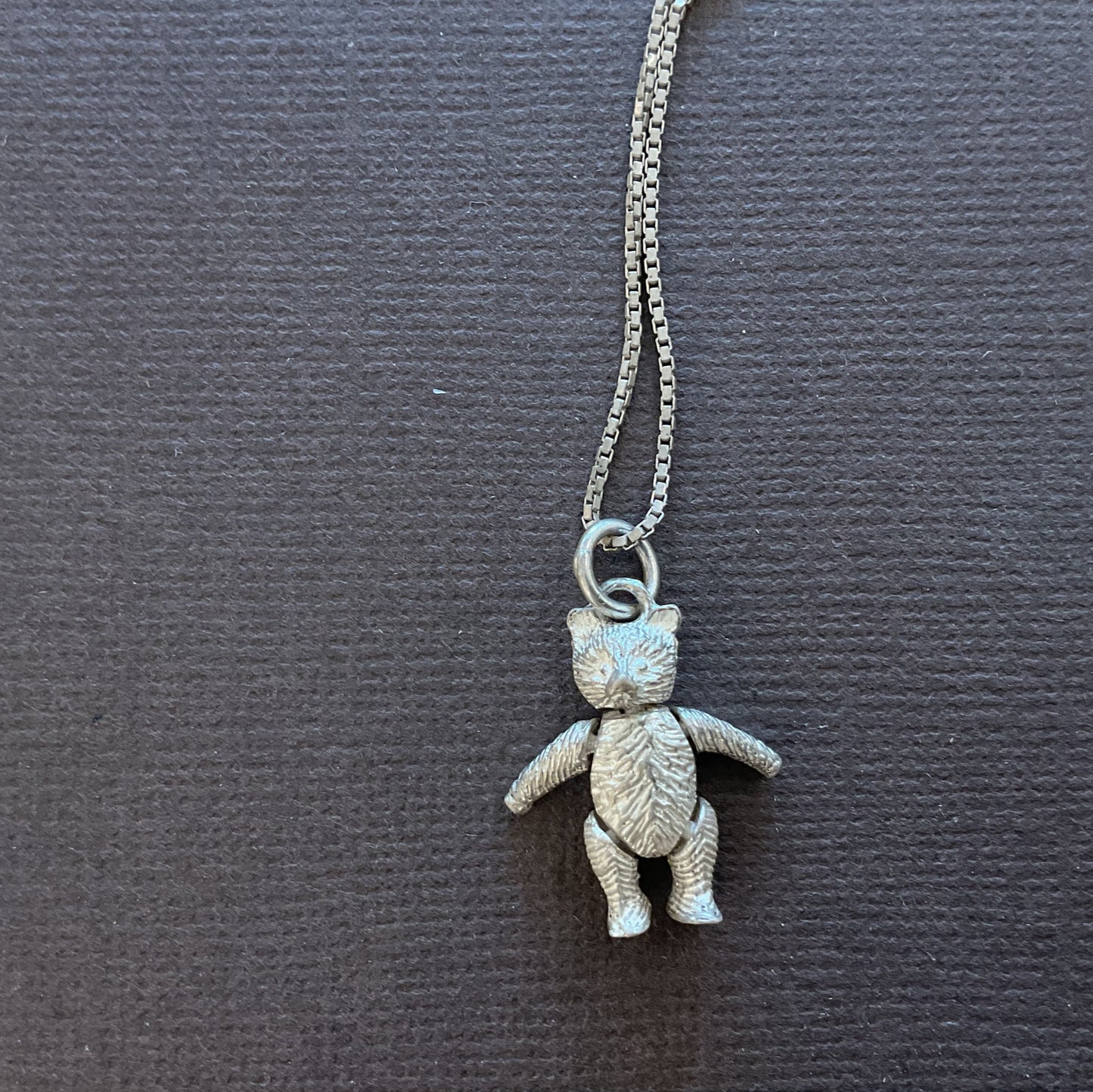 Silver teddy bear pendant necklace on a dark card with text
