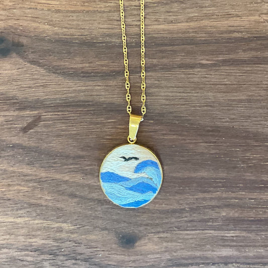 Gold necklace with a pendant featuring a blue design on a wooden surface