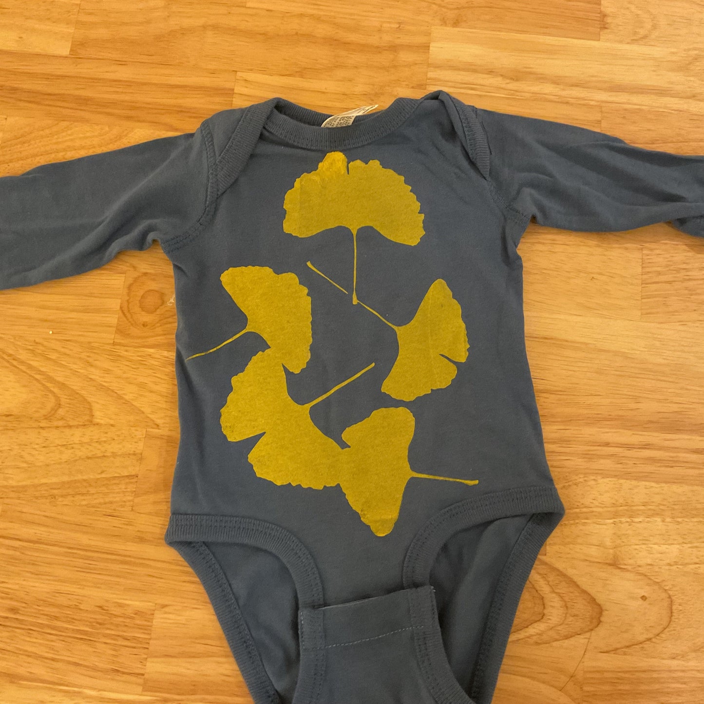 Gray baby onesie with yellow leaf design on a wooden floor