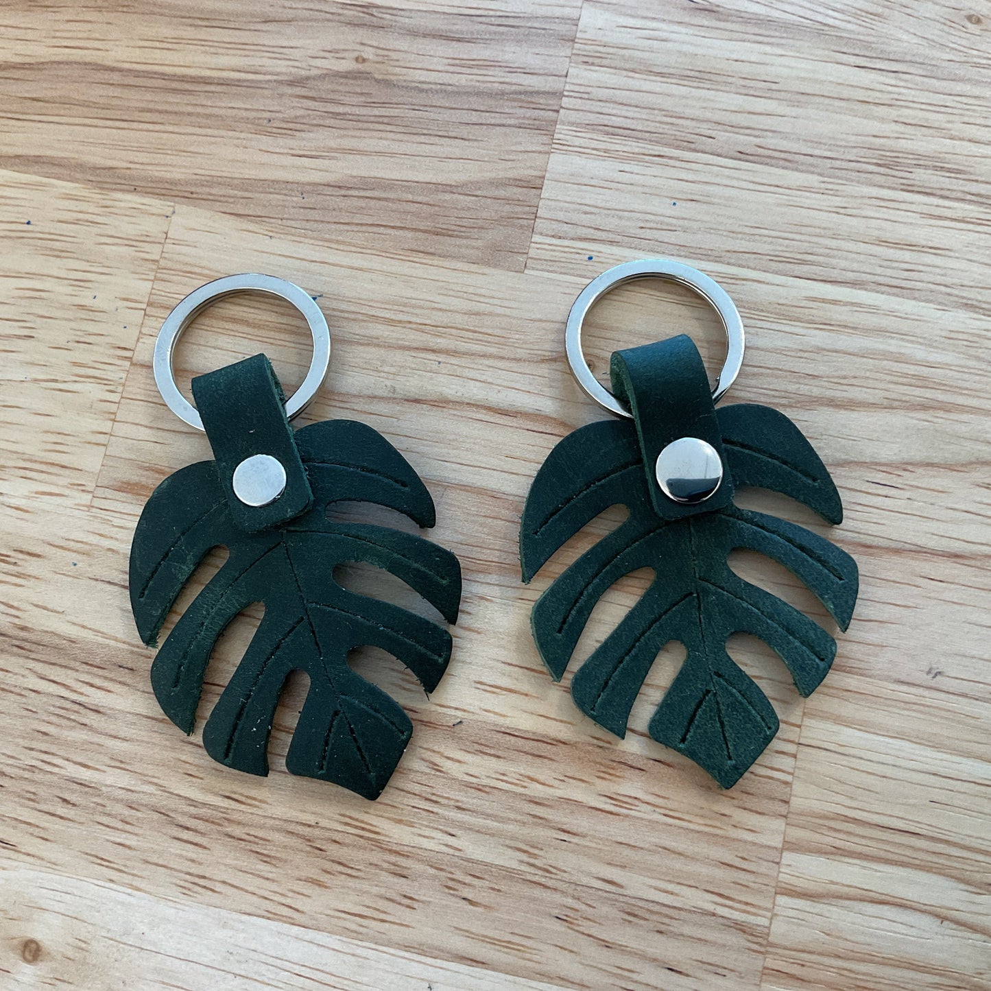 Two green leaf-shaped keychains on a wooden surface