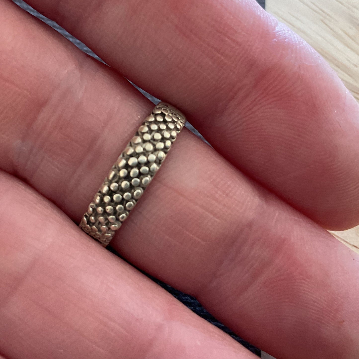 Gold ring on a finger with a light wooden background