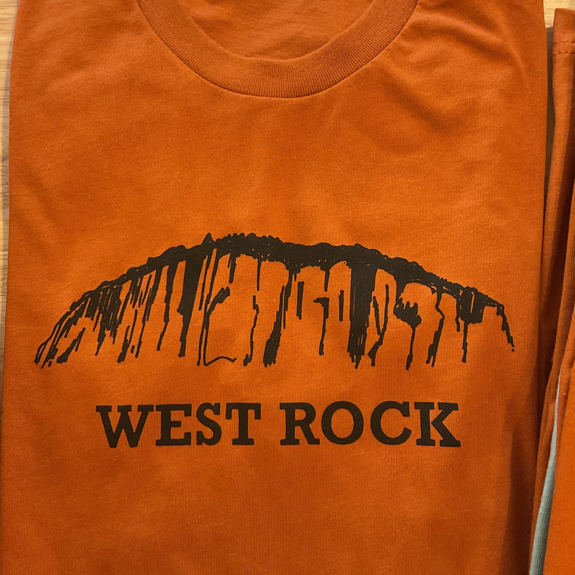 Orange t-shirt with 'West Rock' logo on a wooden surface