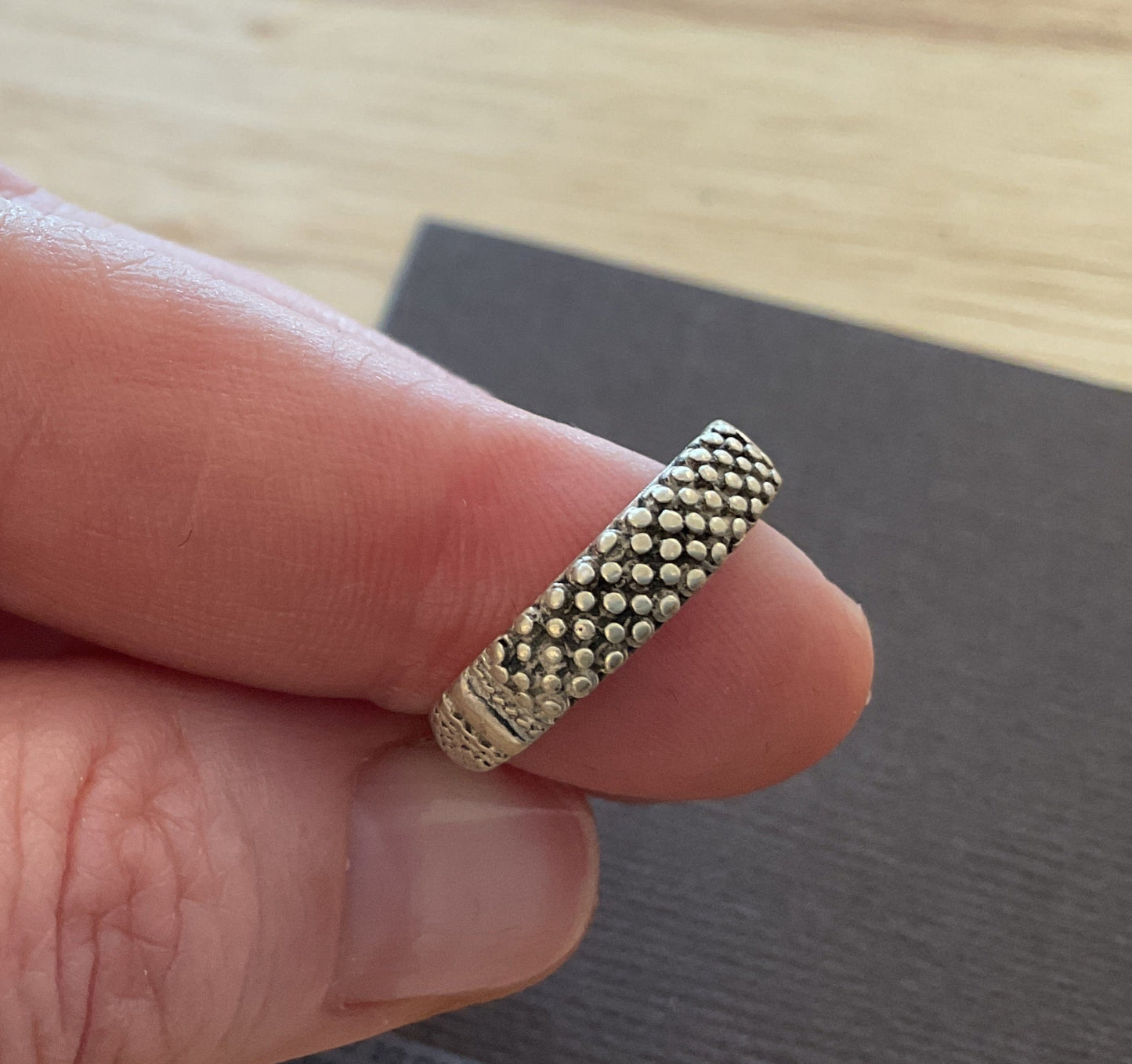Hand holding a textured gold ring on a wooden surface