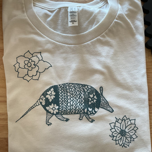 White t-shirt with black armadillo and flower design on a wooden surface