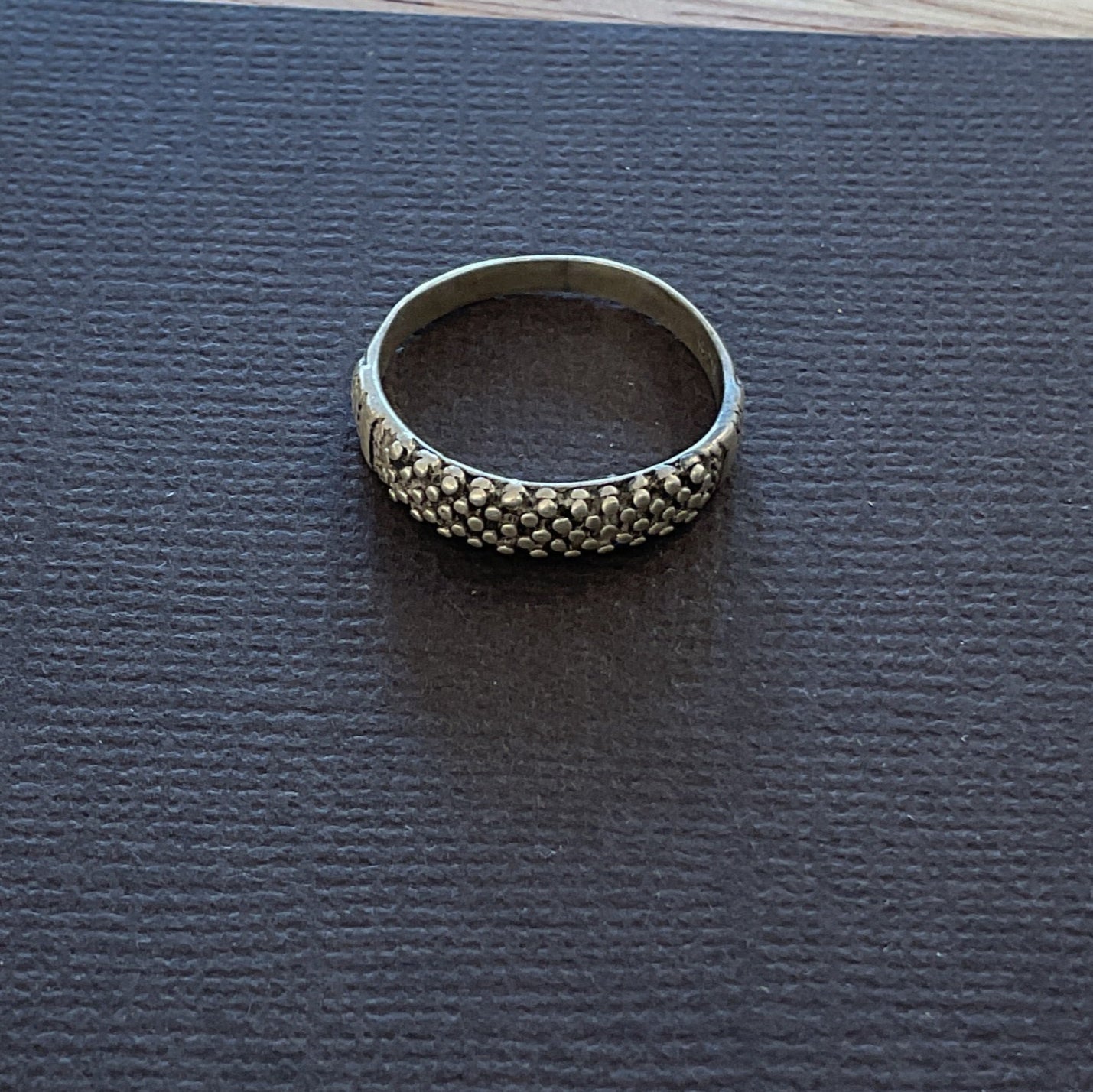 Silver ring on a textured black square mat on a wooden surface