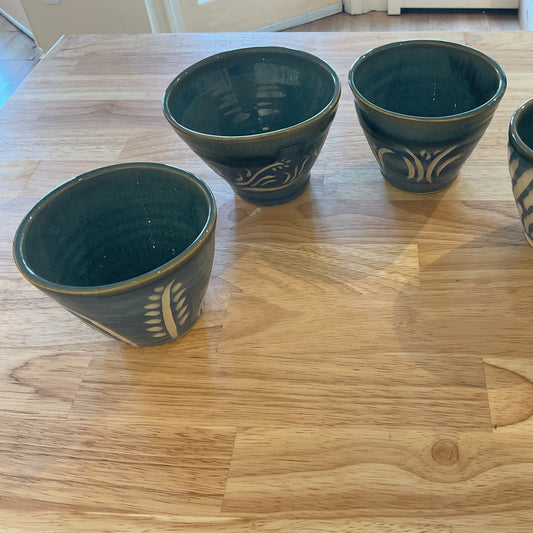 Four green ceramic cups with patterns on a wooden table