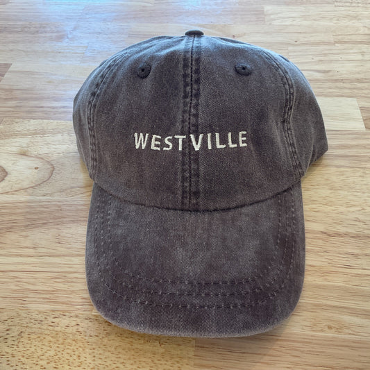 Brown cap with 'WESTVILLE' text on a wooden surface