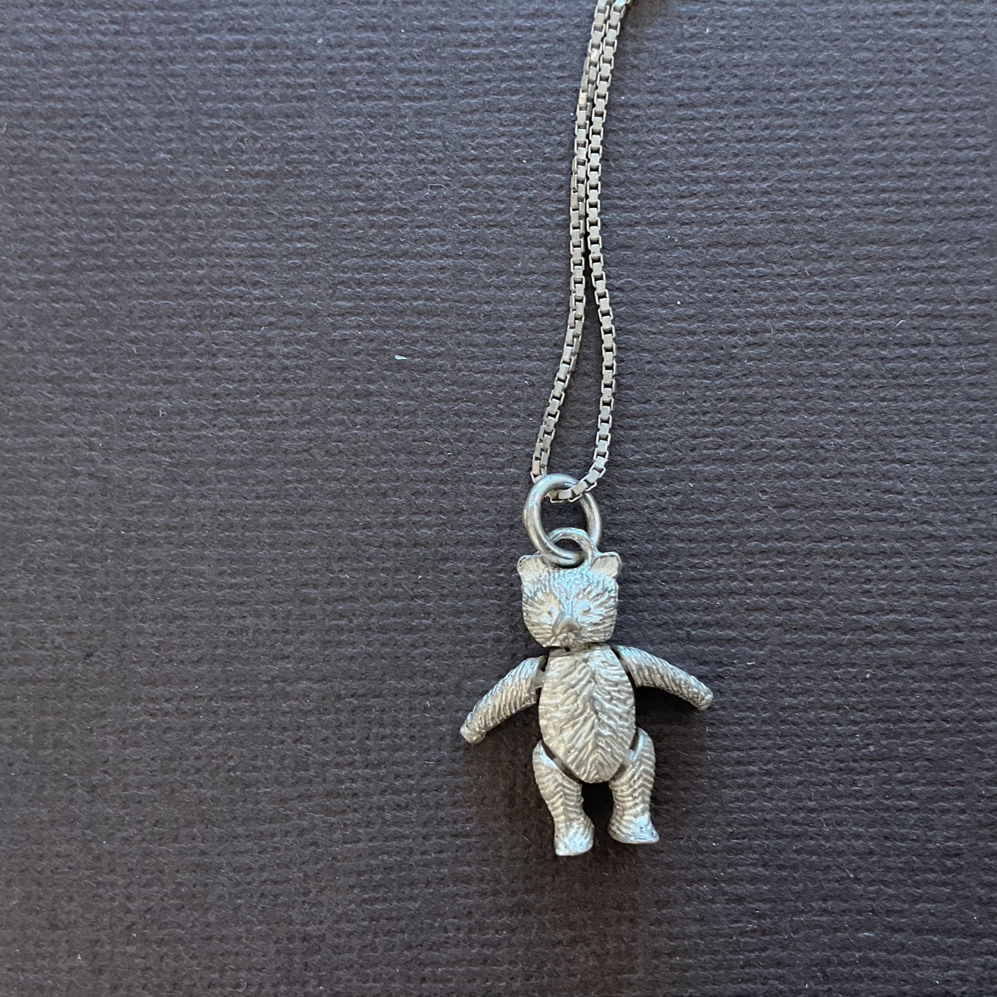 Silver teddy bear pendant necklace on a dark card with text