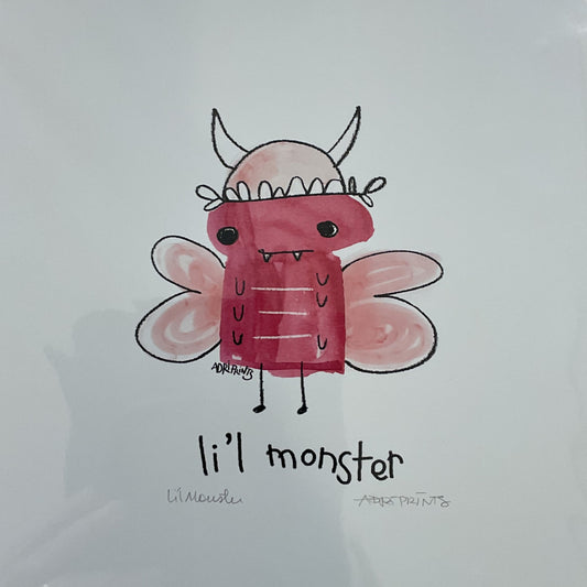 Print of a pink 'li'l monster' illustration on a wooden surface