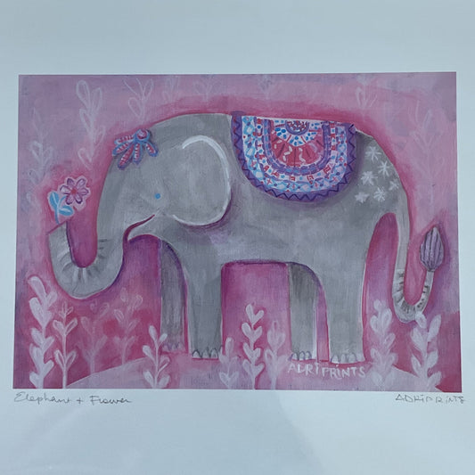 Decorative print of an elephant on a pink background, framed in clear plastic on a wooden surface.