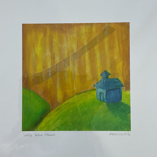 Framed artwork of a blue house on a green hill with a brown path on a wooden floor.
