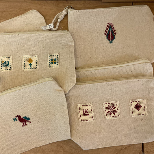 Set of beige pouches with embroidered designs on a wooden surface