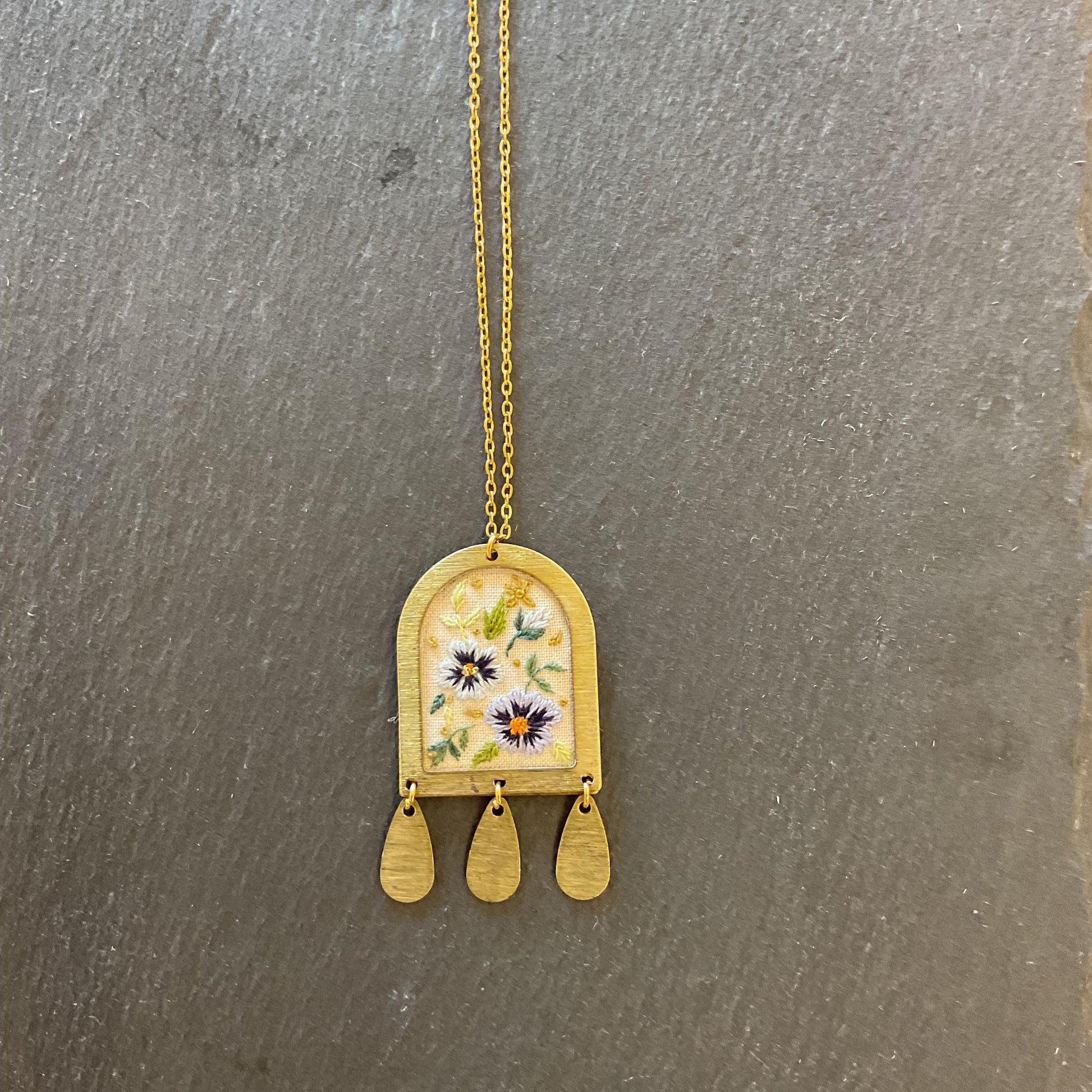 Gold necklace with a floral pendant on a gray surface