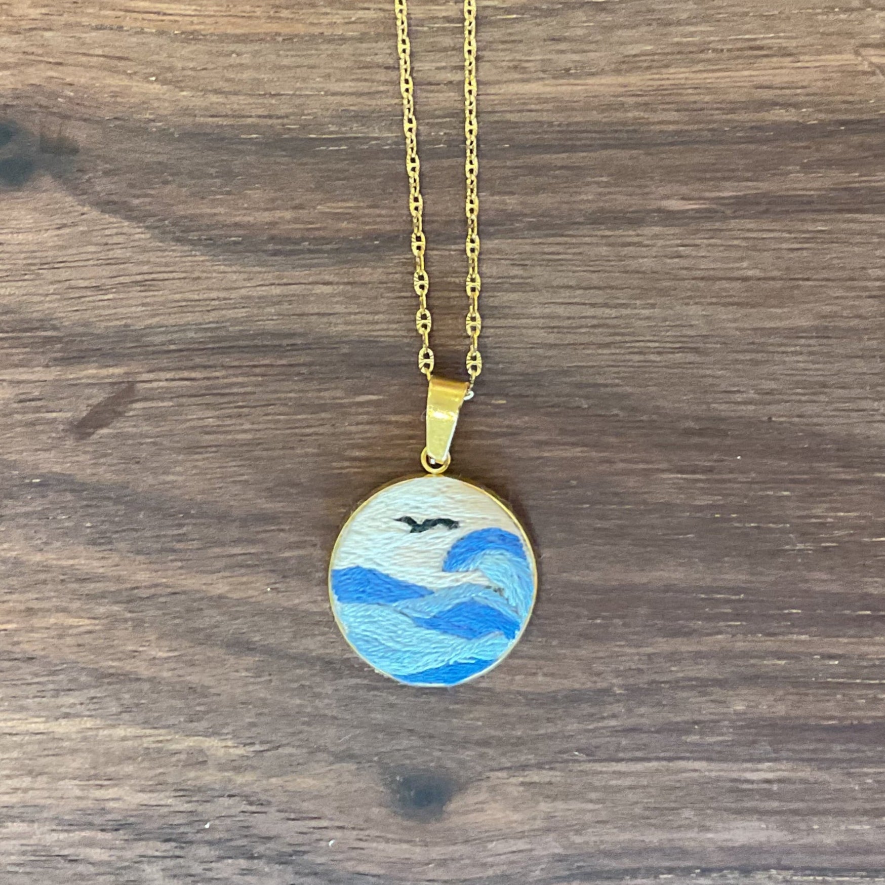 Gold necklace with a pendant featuring a blue design on a wooden surface
