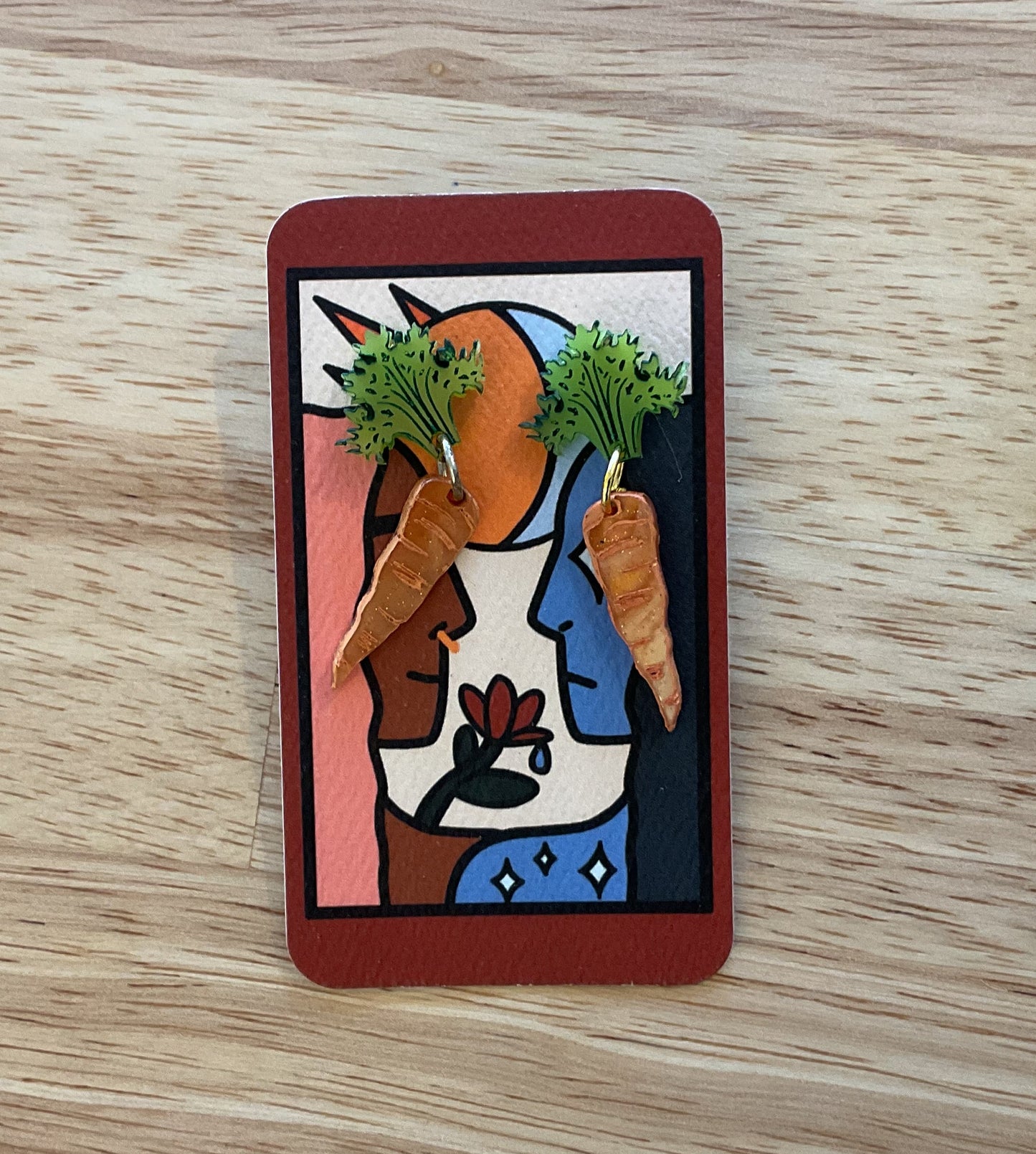 Card with a colorful design featuring a face, carrots, and a cat on a wooden surface