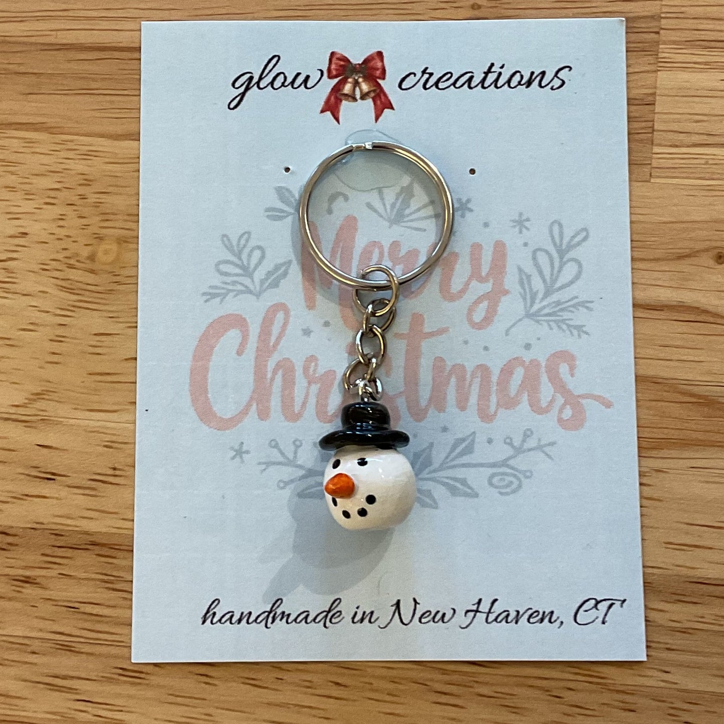 Snowman keychain on a 'Glow Creations' card with 'Merry Christmas' text on a wooden surface