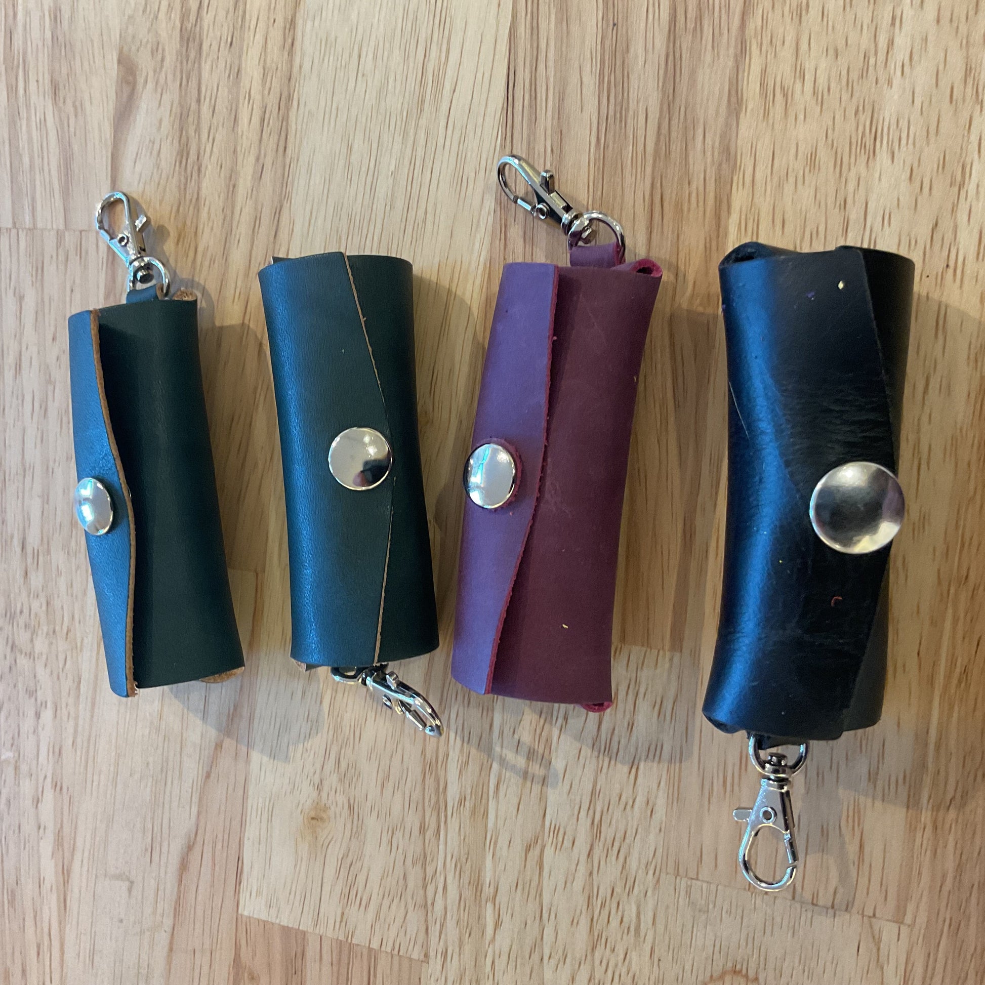 Four leather key cases in black, blue, purple, and black on a wooden surface.
