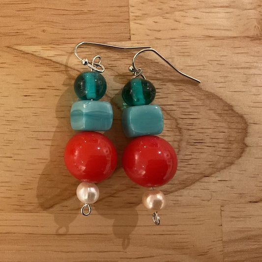 Pair of earrings with red, green, and blue beads on a wooden surface
