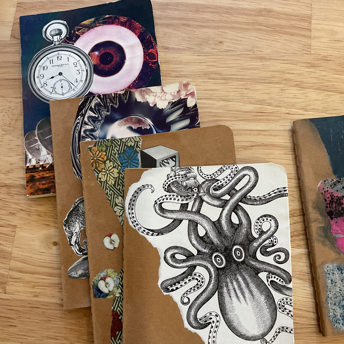 A stack of handmade collage cards or postcards on a light wood floor. The top card features a black ink octopus illustration on a white background, layered over brown kraft paper and other mixed-media pieces including a pocket watch and floral imagery.