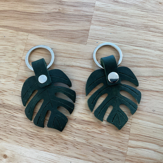 Two green leaf-shaped keychains on a wooden surface