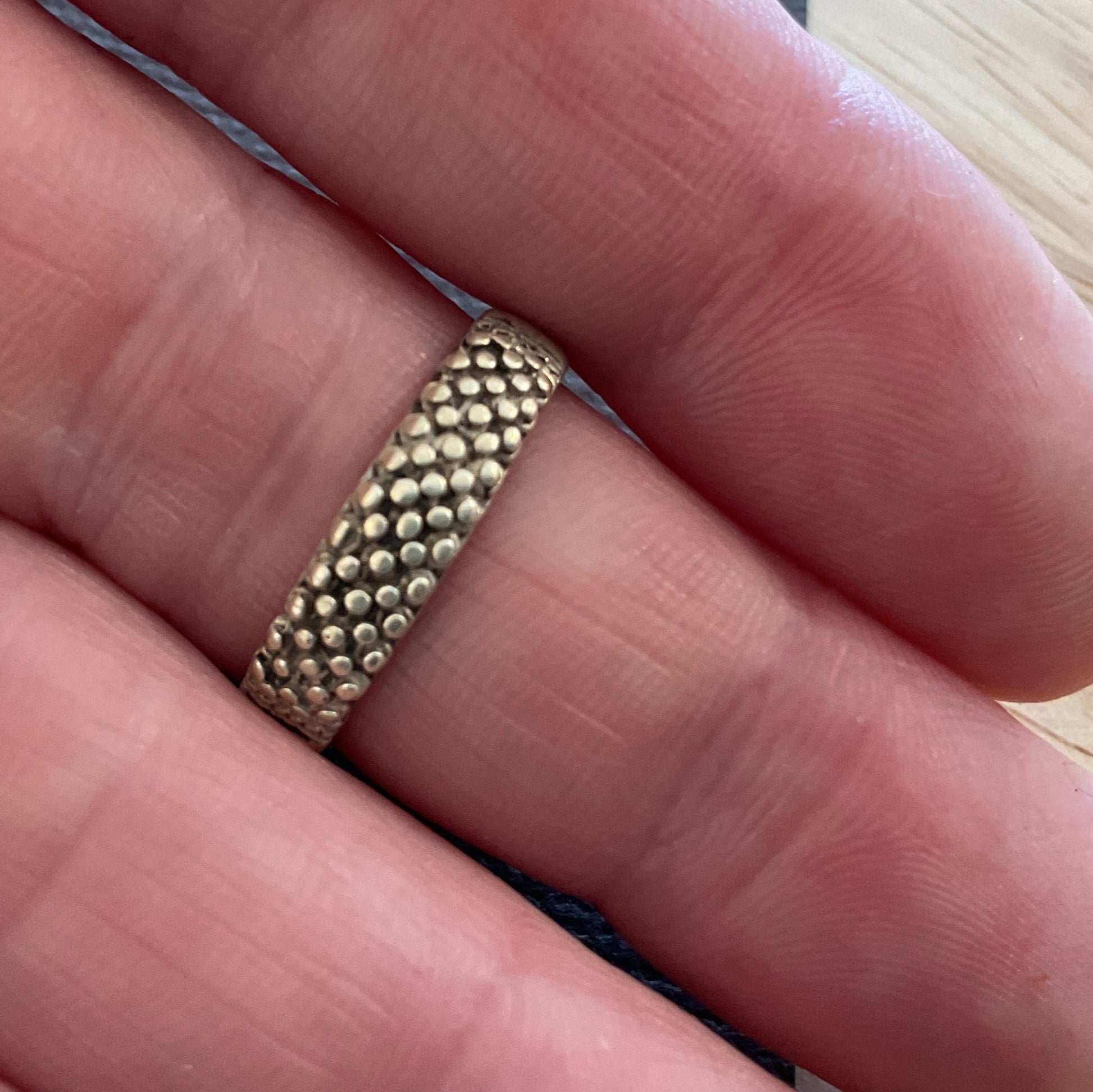 Gold ring on a finger with a light wooden background