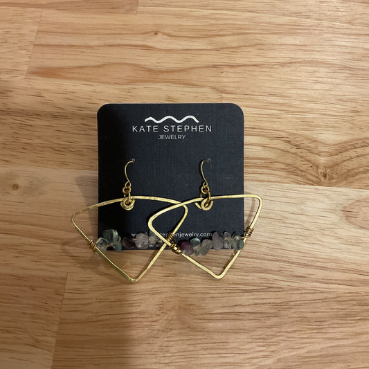 Gold earrings on a black card with 'Katerina' branding on a wooden surface