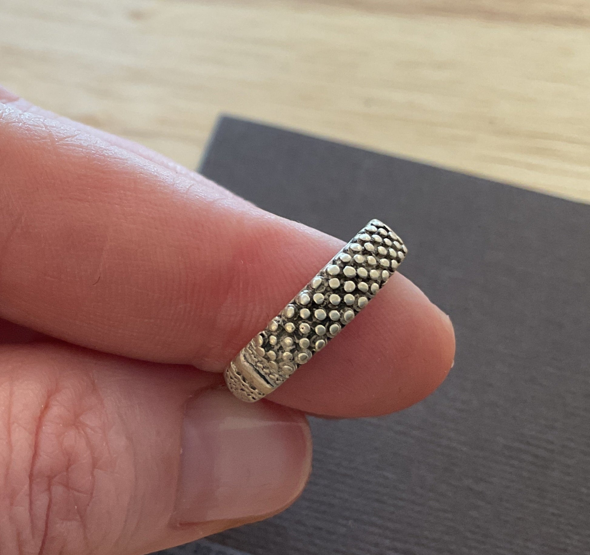 Hand holding a textured gold ring on a wooden surface