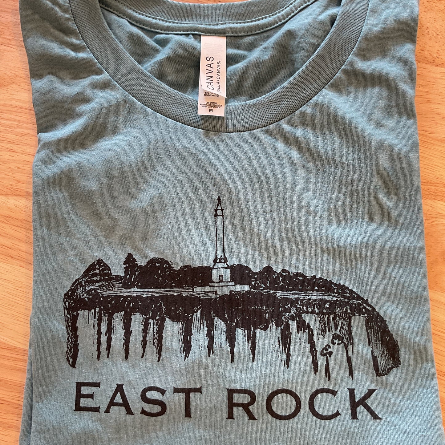 Gray t-shirt with 'East Rock' graphic design on a wooden surface